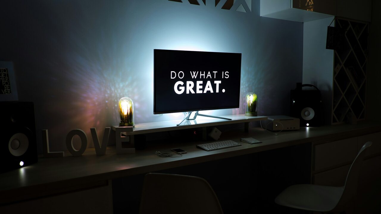 A desk setup with a screen displaying Do what is great.